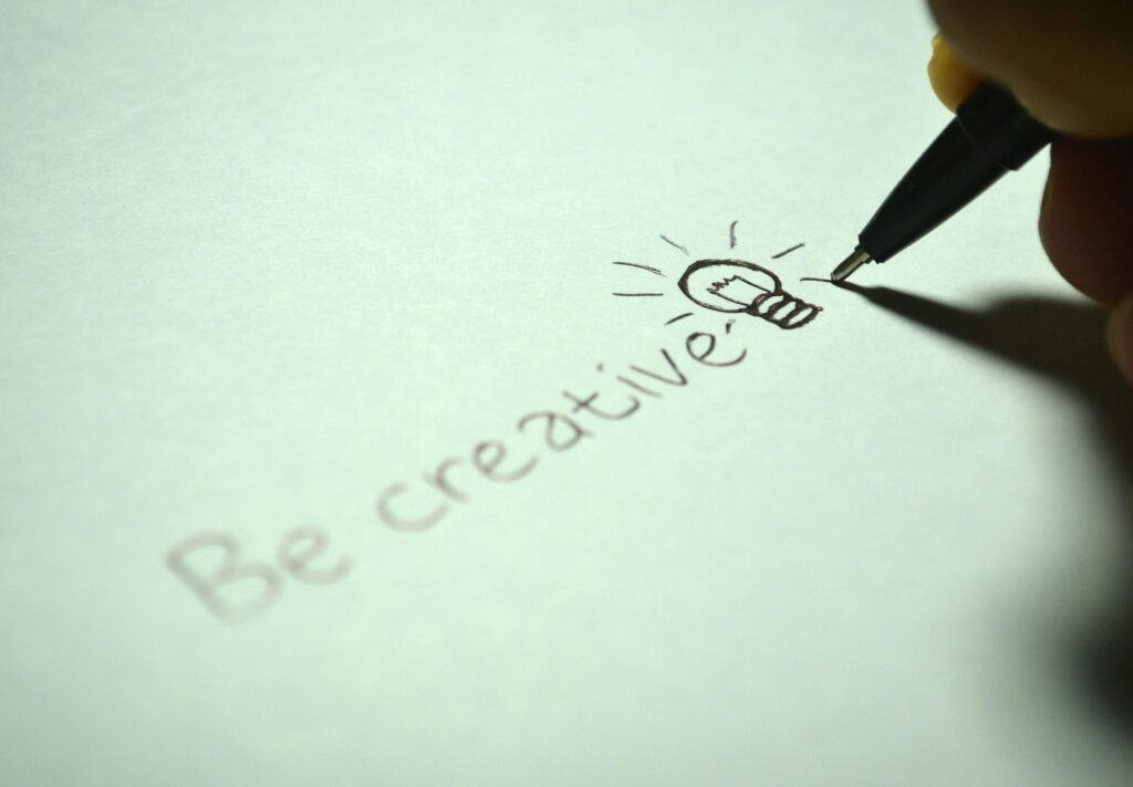 pexels-photo-256514-256514 Close-up of handwritten 'Be creative' with a light bulb sketch on paper.